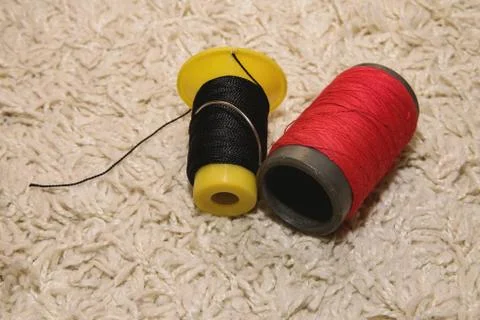 Two spools of red and black thread with a needle lies on a white background Stock Photos