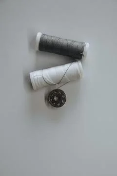 Two spools of white and gray thread and a button lie on a light background Foto stock