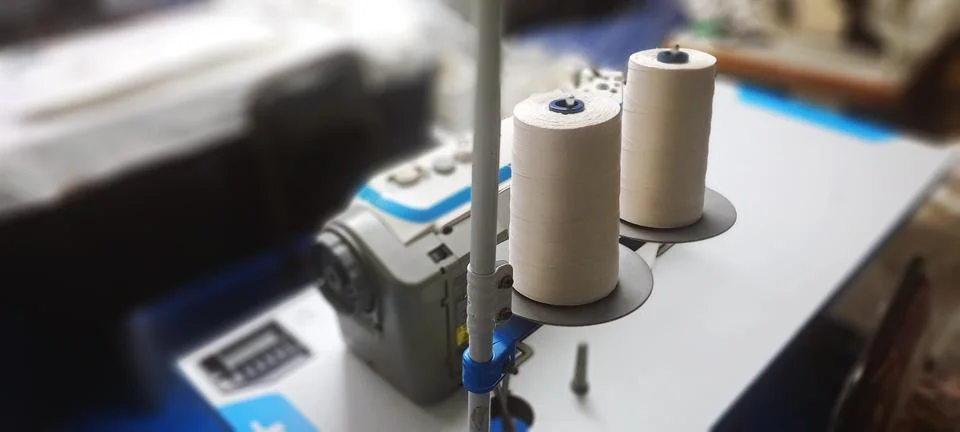 Two spools of white thread standing on sewing machine in workshop Stock Photos