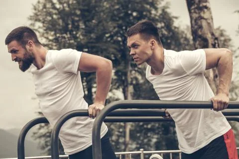 Two sportsmen doing dips on parallel bars Stock Photos