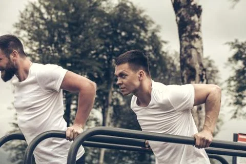 Two sportsmen doing dips on parallel bars Stock Photos