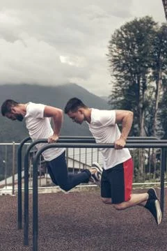 Two sportsmen doing dips on parallel bars Stock Photos