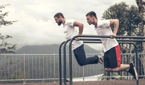 Two sportsmen doing dips on parallel bars Stock Photos