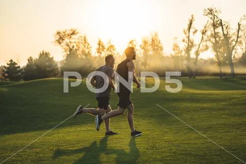 The two sportsmen running on the grass in the park on the sunny background Stock Photos