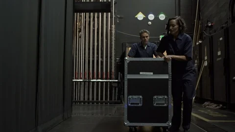 Two stage workers wheeling equipment trolley towards camera, backstage 스톡 동영상 88037915