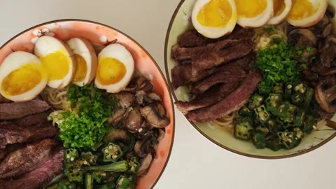 Two steaming bowls of ramen noodle soup with steak and egg Stock Footage 340896541