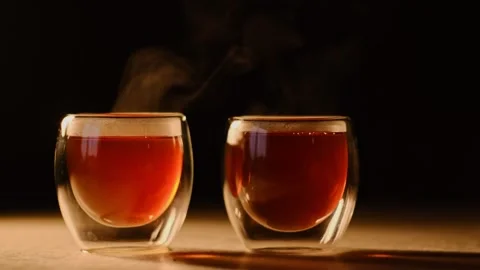 Two steaming tea cups on a dark background, with warm lighting emphasizing the Vídeo Stock 295633885