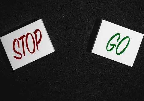 Two sticky notes on a black background with Stop and go written on it Stock Photos