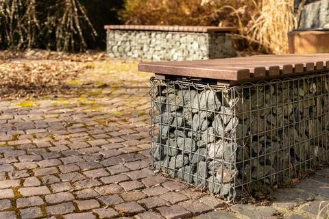 Two stone benches sit on a cobblestone path surrounded by dry plants. The a.. Stock Photos