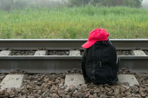 Two straps backpack , red cap next to railroad tracks against blurred meadow. Stock-Fotos
