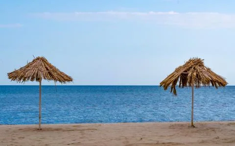 Two straw beach umbrellas on an empty seashore on a clear day Stock-Fotos