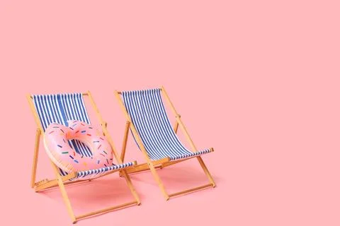 Two striped deck chairs with pink donut float on pink background Stock Photos