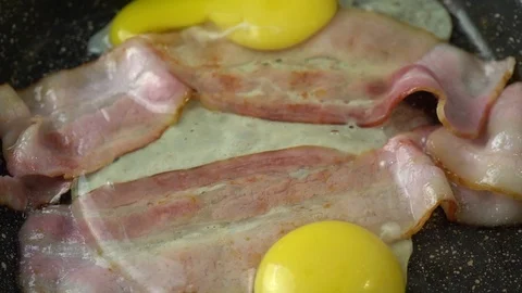 Two strips of bacon frying in a pan with two eggs Stock Footage 125930918