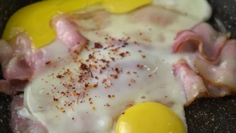 Two strips of bacon, two eggs with spices frying in a pan Stock Footage 125931696