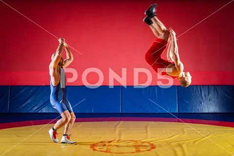 Two strong wrestlers in blue and red tights make flips and jumps on the yello Stock Photos
