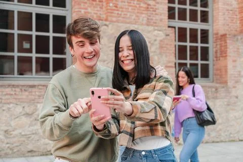 Two student people having fun with a mobile phone outdoors. Young friends b.. Stock Photos
