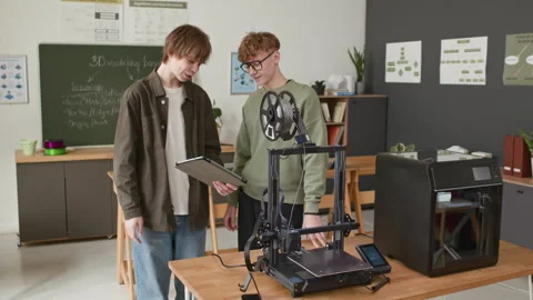 Two Students in 3D Modeling Class Discussing Project Near 3D Printers Stock Footage 335691486