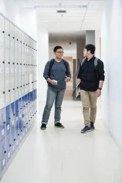 Two students are standing next to lockers and talking together down the hall Stock Photos