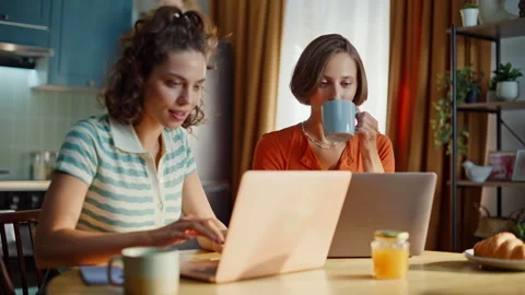 Two students browsing laptops sitting at home kitchen closeup. Positive women Stock Footage 333776439