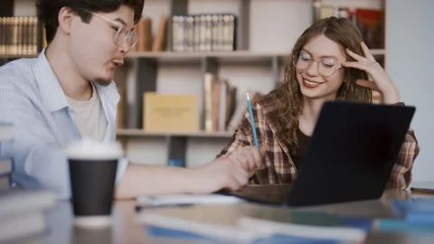 Two students collaborate on a laptop during focused study in a quiet library Stock Footage 341337235