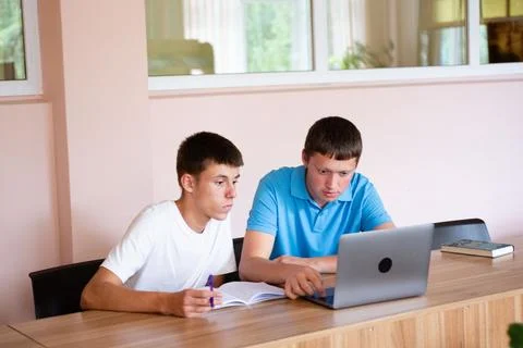 Two students collaborate on a project together, using a laptop and taking n.. Stock Photos