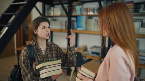 Two students discuss and share books in a library during the day while standing  Stock Footage 331749299