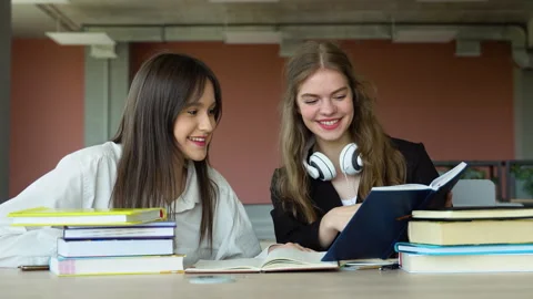 Two students doing homework together and helping each other sitting in a table Stock Footage 243322694
