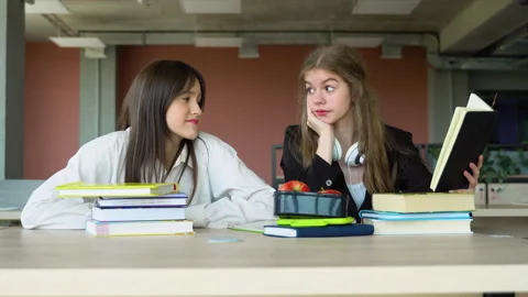 Two students doing homework together and helping each other sitting in a table 스톡 동영상 243322739
