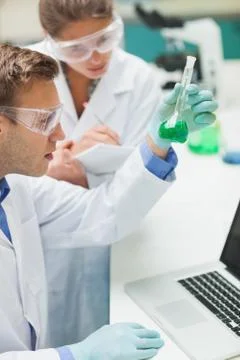 Two students examining green liquid and taking notes 写真素材