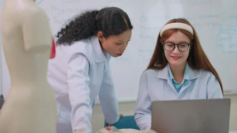 Two students in lab coats collaborate near a laptop Stock Footage 339406266