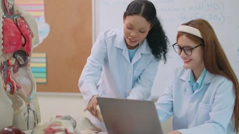 Two students in lab coats collaborate near a laptop Stock Footage 339406547
