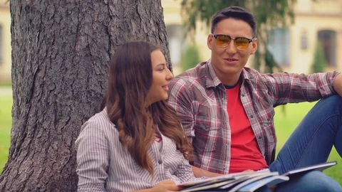 Two students leaned on a tree talking reading a book Stock Footage 126722250