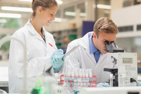 Two students looking through microscope and taking notes Stock Photos