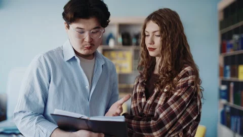 Two students reading and discussing a textbook in a library with focused Stock-Footage 346892231
