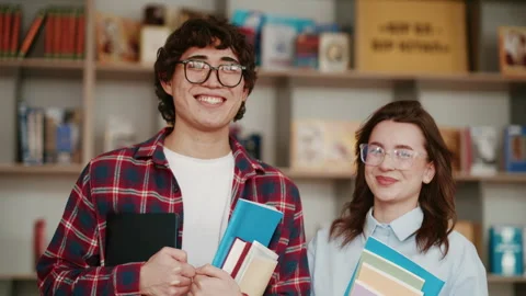 Two students smiling with books in a library, showcasing friendship and learning Stock Footage 341646086