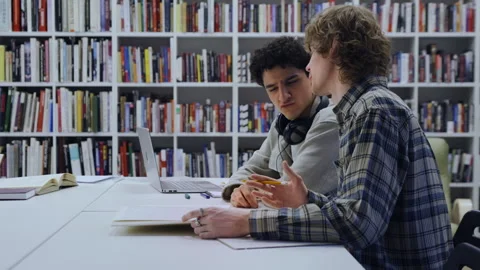 Two Students Talking and Working on Homework as Another Browses a Bookshelf Stock Footage 335140865