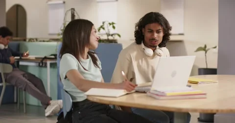 Two students working in study hub, man approaching to discuss laptop while woman Stock Footage 337705381