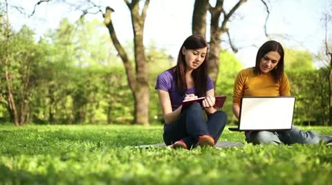 Two students working together with book and laptop outside, tracking shot HD Stock Footage 11055803