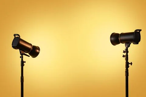 Two studio strobe lights on stands illuminating a warm yellow gradient backgr Stock Photos