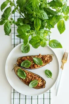 Two stuffed eggplant halves presented on white plate with fresh basil garni.. Stock Photos