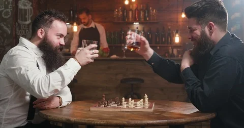 Two stylish men having a conversation over a glass of whiskey and a chess game Stockbeeldmateriaal 103859673