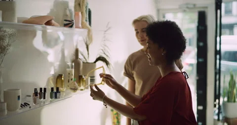 Two stylish women looking at display and trying on sunglasses in interior boutiq Stock Footage 199457682