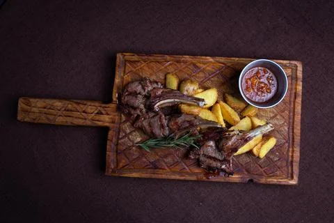 Two succulent lamb chops and crispy potato wedges served on a rustic wooden b Stock Photos