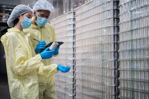 Two supervisors inspect quality of containers in canned food manufacturing. Stock Photos