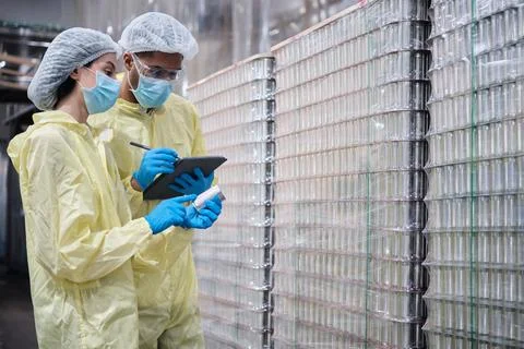 Two supervisors inspect quality of containers in canned food manufacturing. Stock Photos