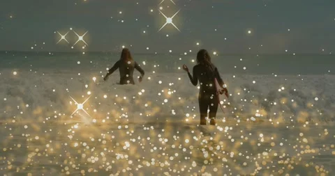 Two surfers stepping into waves seeking surf right holding board, golden bokeh Stock Footage 331272611