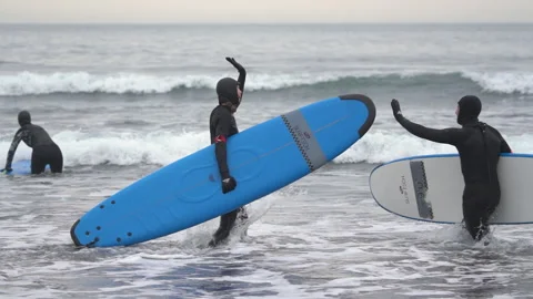 Two surfers with surfboard walking in wave Pacific Ocean, saluting high five Stock Footage 249713399