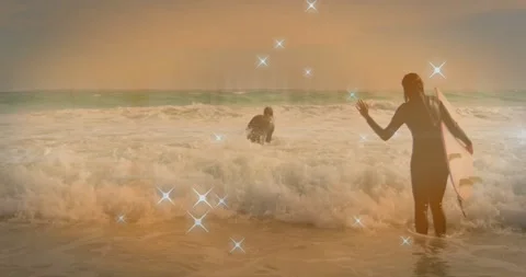 Two surfers wading and bracing with board stepping into surf, sparkle overlay Stock Footage 331269699