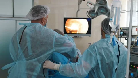 Two surgeons and a nurse in lab coats and masks perform endoscopic surgery Stock Footage 132766247