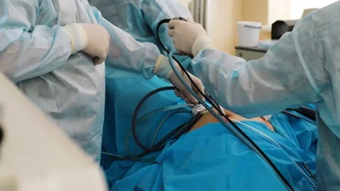Two surgeons in lab coats and an assistant perform endoscopic surgery Stock Footage 132748595